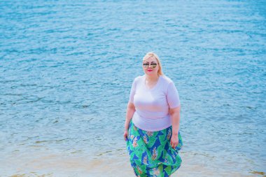 Artı plajda bir model. Şişman kadın hayattan zevk alıyor. Nehir kenarındaki doğada, kumların üzerinde dinlenen güzel bir kadın. Kadın hayatı kavramı.