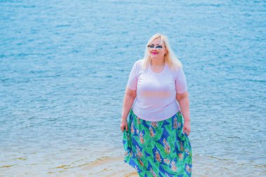 Artı plajda bir model. Şişman kadın hayattan zevk alıyor. Nehir kenarındaki doğada, kumların üzerinde dinlenen güzel bir kadın. Kadın hayatı kavramı.