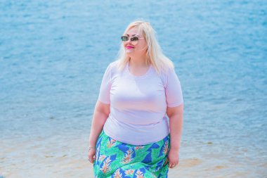 Artı plajda bir model. Şişman kadın hayattan zevk alıyor. Nehir kenarındaki doğada, kumların üzerinde dinlenen güzel bir kadın. Kadın hayatı kavramı.