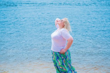 Artı plajda bir model. Şişman kadın hayattan zevk alıyor. Nehir kenarındaki doğada, kumların üzerinde dinlenen güzel bir kadın. Kadın hayatı kavramı.