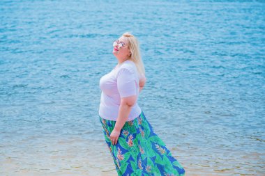 Artı plajda bir model. Şişman kadın hayattan zevk alıyor. Nehir kenarındaki doğada, kumların üzerinde dinlenen güzel bir kadın. Kadın hayatı kavramı.