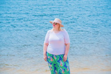 Artı plajda bir model. Şişman kadın hayattan zevk alıyor. Nehir kenarındaki doğada, kumların üzerinde dinlenen güzel bir kadın. Kadın hayatı kavramı.