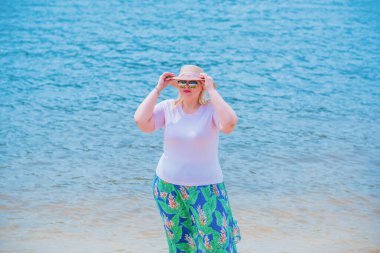 Artı plajda bir model. Şişman kadın hayattan zevk alıyor. Nehir kenarındaki doğada, kumların üzerinde dinlenen güzel bir kadın. Kadın hayatı kavramı.