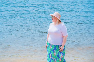 Artı plajda bir model. Şişman kadın hayattan zevk alıyor. Nehir kenarındaki doğada, kumların üzerinde dinlenen güzel bir kadın. Kadın hayatı kavramı.