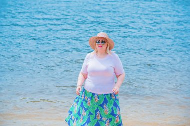 Artı plajda bir model. Şişman kadın hayattan zevk alıyor. Nehir kenarındaki doğada, kumların üzerinde dinlenen güzel bir kadın. Kadın hayatı kavramı.