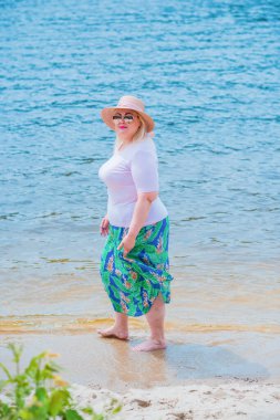 Artı plajda bir model. Şişman kadın hayattan zevk alıyor. Nehir kenarındaki doğada, kumların üzerinde dinlenen güzel bir kadın. Kadın hayatı kavramı.