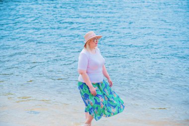 Artı plajda bir model. Şişman kadın hayattan zevk alıyor. Nehir kenarındaki doğada, kumların üzerinde dinlenen güzel bir kadın. Kadın hayatı kavramı.