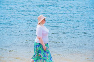 Artı plajda bir model. Şişman kadın hayattan zevk alıyor. Nehir kenarındaki doğada, kumların üzerinde dinlenen güzel bir kadın. Kadın hayatı kavramı.