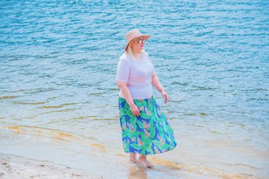 Artı plajda bir model. Şişman kadın hayattan zevk alıyor. Nehir kenarındaki doğada, kumların üzerinde dinlenen güzel bir kadın. Kadın hayatı kavramı.