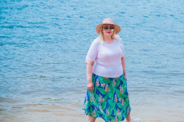 Artı plajda bir model. Şişman kadın hayattan zevk alıyor. Nehir kenarındaki doğada, kumların üzerinde dinlenen güzel bir kadın. Kadın hayatı kavramı.