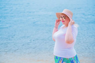 Artı plajda bir model. Şişman kadın hayattan zevk alıyor. Nehir kenarındaki doğada, kumların üzerinde dinlenen güzel bir kadın. Kadın hayatı kavramı.