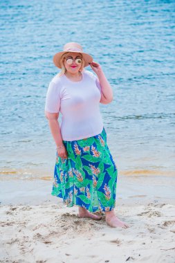 Artı plajda bir model. Şişman kadın hayattan zevk alıyor. Nehir kenarındaki doğada, kumların üzerinde dinlenen güzel bir kadın. Kadın hayatı kavramı.