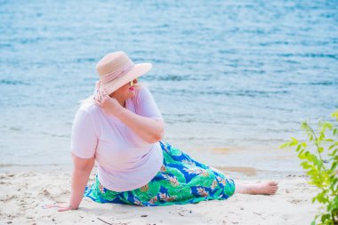 Artı plajda bir model. Şişman kadın hayattan zevk alıyor. Nehir kenarındaki doğada, kumların üzerinde dinlenen güzel bir kadın. Kadın hayatı kavramı.