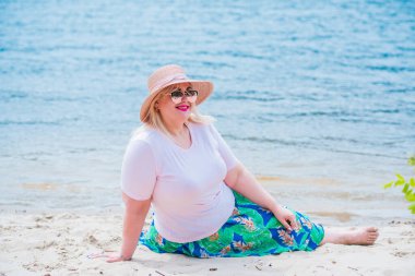 Artı plajda bir model. Şişman kadın hayattan zevk alıyor. Nehir kenarındaki doğada, kumların üzerinde dinlenen güzel bir kadın. Kadın hayatı kavramı.