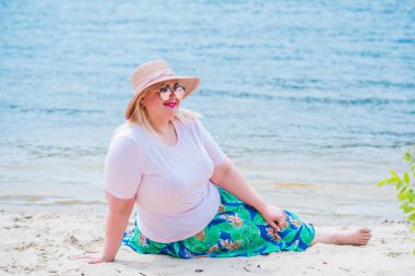 Artı plajda bir model. Şişman kadın hayattan zevk alıyor. Nehir kenarındaki doğada, kumların üzerinde dinlenen güzel bir kadın. Kadın hayatı kavramı.