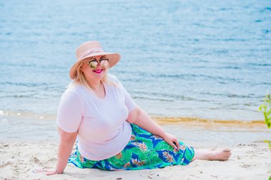 Artı plajda bir model. Şişman kadın hayattan zevk alıyor. Nehir kenarındaki doğada, kumların üzerinde dinlenen güzel bir kadın. Kadın hayatı kavramı.