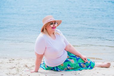 Artı plajda bir model. Şişman kadın hayattan zevk alıyor. Nehir kenarındaki doğada, kumların üzerinde dinlenen güzel bir kadın. Kadın hayatı kavramı.