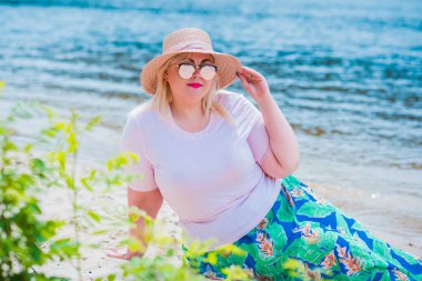 Artı plajda bir model. Şişman kadın hayattan zevk alıyor. Nehir kenarındaki doğada, kumların üzerinde dinlenen güzel bir kadın. Kadın hayatı kavramı.