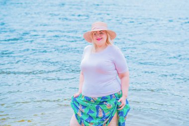 Artı plajda bir model. Şişman kadın hayattan zevk alıyor. Nehir kenarındaki doğada, kumların üzerinde dinlenen güzel bir kadın. Kadın hayatı kavramı.