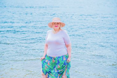 Artı plajda bir model. Şişman kadın hayattan zevk alıyor. Nehir kenarındaki doğada, kumların üzerinde dinlenen güzel bir kadın. Kadın hayatı kavramı.