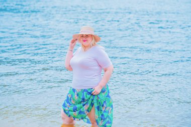 Artı plajda bir model. Şişman kadın hayattan zevk alıyor. Nehir kenarındaki doğada, kumların üzerinde dinlenen güzel bir kadın. Kadın hayatı kavramı.