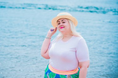 Artı plajda bir model. Şişman kadın hayattan zevk alıyor. Nehir kenarındaki doğada, kumların üzerinde dinlenen güzel bir kadın. Kadın hayatı kavramı.