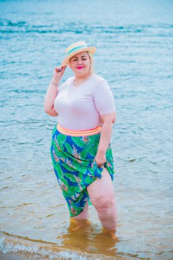 Artı plajda bir model. Şişman kadın hayattan zevk alıyor. Nehir kenarındaki doğada, kumların üzerinde dinlenen güzel bir kadın. Kadın hayatı kavramı.