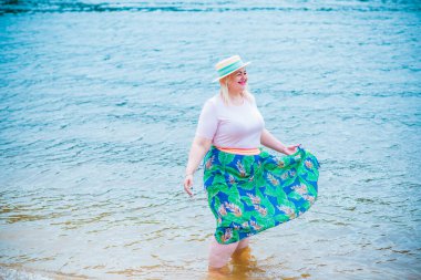 Artı plajda bir model. Şişman kadın hayattan zevk alıyor. Nehir kenarındaki doğada, kumların üzerinde dinlenen güzel bir kadın. Kadın hayatı kavramı.