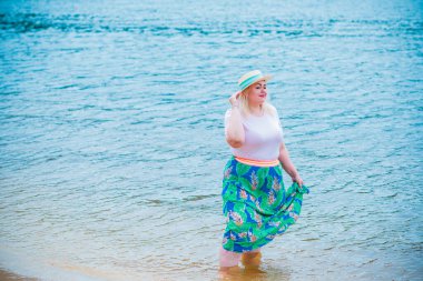 Artı plajda bir model. Şişman kadın hayattan zevk alıyor. Nehir kenarındaki doğada, kumların üzerinde dinlenen güzel bir kadın. Kadın hayatı kavramı.