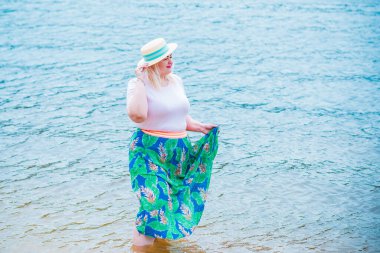 Artı plajda bir model. Şişman kadın hayattan zevk alıyor. Nehir kenarındaki doğada, kumların üzerinde dinlenen güzel bir kadın. Kadın hayatı kavramı.