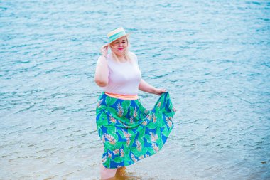 Artı plajda bir model. Şişman kadın hayattan zevk alıyor. Nehir kenarındaki doğada, kumların üzerinde dinlenen güzel bir kadın. Kadın hayatı kavramı.