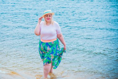 Artı plajda bir model. Şişman kadın hayattan zevk alıyor. Nehir kenarındaki doğada, kumların üzerinde dinlenen güzel bir kadın. Kadın hayatı kavramı.