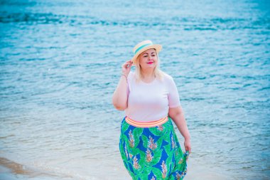 Artı plajda bir model. Şişman kadın hayattan zevk alıyor. Nehir kenarındaki doğada, kumların üzerinde dinlenen güzel bir kadın. Kadın hayatı kavramı.