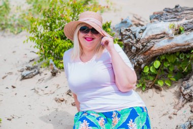 Artı plajda bir model. Şişman kadın hayattan zevk alıyor. Nehir kenarındaki doğada, kumların üzerinde dinlenen güzel bir kadın. Kadın hayatı kavramı.