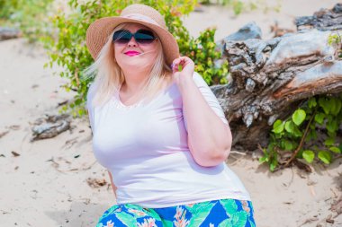 Artı plajda bir model. Şişman kadın hayattan zevk alıyor. Nehir kenarındaki doğada, kumların üzerinde dinlenen güzel bir kadın. Kadın hayatı kavramı.