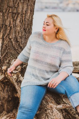 Artı plajda bir model. Şişman kadın hayattan zevk alıyor. Nehir kenarındaki doğada, kumların üzerinde dinlenen güzel bir kadın. Kadın hayatı kavramı.