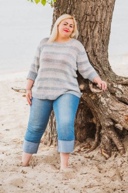 Artı plajda bir model. Şişman kadın hayattan zevk alıyor. Nehir kenarındaki doğada, kumların üzerinde dinlenen güzel bir kadın. Kadın hayatı kavramı.