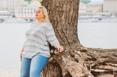 Artı plajda bir model. Şişman kadın hayattan zevk alıyor. Nehir kenarındaki doğada, kumların üzerinde dinlenen güzel bir kadın. Kadın hayatı kavramı.