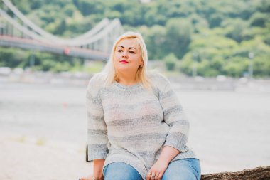 Artı plajda bir model. Şişman kadın hayattan zevk alıyor. Nehir kenarındaki doğada, kumların üzerinde dinlenen güzel bir kadın. Kadın hayatı kavramı.