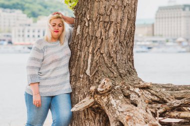 Artı plajda bir model. Şişman kadın hayattan zevk alıyor. Nehir kenarındaki doğada, kumların üzerinde dinlenen güzel bir kadın. Kadın hayatı kavramı.