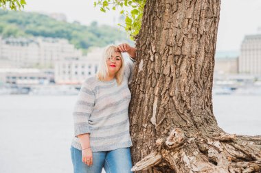 Artı plajda bir model. Şişman kadın hayattan zevk alıyor. Nehir kenarındaki doğada, kumların üzerinde dinlenen güzel bir kadın. Kadın hayatı kavramı.