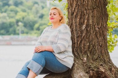 Artı plajda bir model. Şişman kadın hayattan zevk alıyor. Nehir kenarındaki doğada, kumların üzerinde dinlenen güzel bir kadın. Kadın hayatı kavramı.