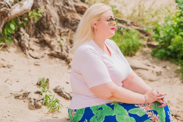 Artı plajda bir model. Şişman kadın hayattan zevk alıyor. Nehir kenarındaki doğada, kumların üzerinde dinlenen güzel bir kadın. Kadın hayatı kavramı.