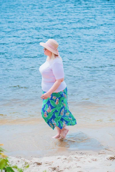 Artı plajda bir model. Şişman kadın hayattan zevk alıyor. Nehir kenarındaki doğada, kumların üzerinde dinlenen güzel bir kadın. Kadın hayatı kavramı.