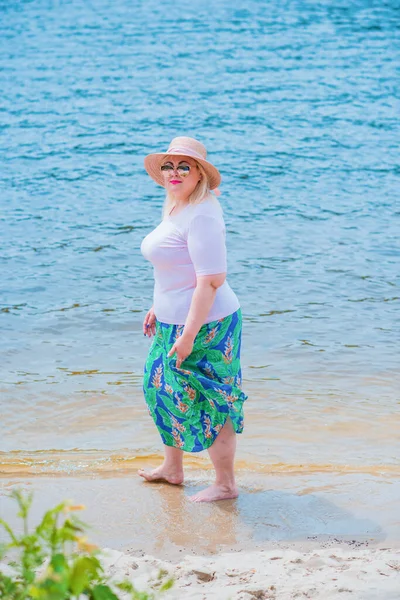 Artı plajda bir model. Şişman kadın hayattan zevk alıyor. Nehir kenarındaki doğada, kumların üzerinde dinlenen güzel bir kadın. Kadın hayatı kavramı.