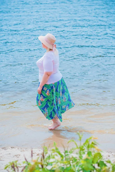 Artı plajda bir model. Şişman kadın hayattan zevk alıyor. Nehir kenarındaki doğada, kumların üzerinde dinlenen güzel bir kadın. Kadın hayatı kavramı.