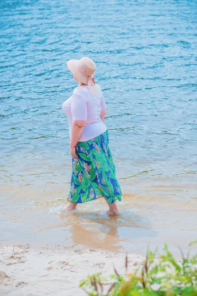 Artı plajda bir model. Şişman kadın hayattan zevk alıyor. Nehir kenarındaki doğada, kumların üzerinde dinlenen güzel bir kadın. Kadın hayatı kavramı.