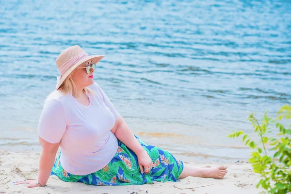 Artı plajda bir model. Şişman kadın hayattan zevk alıyor. Nehir kenarındaki doğada, kumların üzerinde dinlenen güzel bir kadın. Kadın hayatı kavramı.