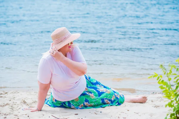 Artı plajda bir model. Şişman kadın hayattan zevk alıyor. Nehir kenarındaki doğada, kumların üzerinde dinlenen güzel bir kadın. Kadın hayatı kavramı.