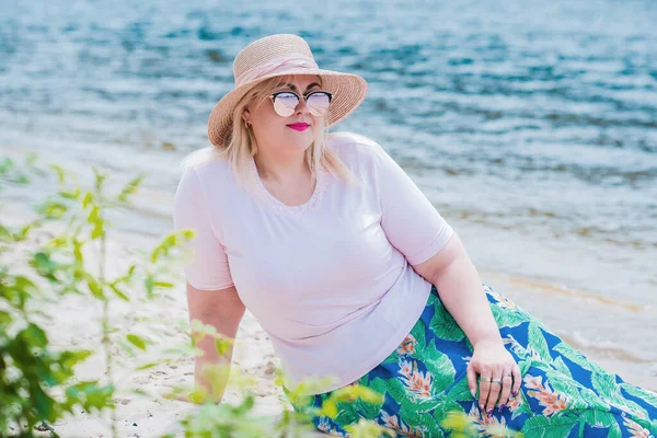 Artı plajda bir model. Şişman kadın hayattan zevk alıyor. Nehir kenarındaki doğada, kumların üzerinde dinlenen güzel bir kadın. Kadın hayatı kavramı.